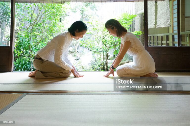 Two Japanese women bowing with respect in a traditional house.