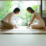 Two Japanese women bowing with respect in a traditional house.