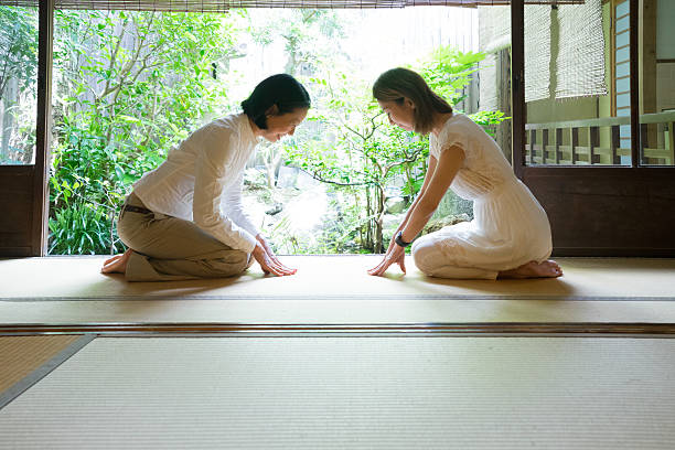 Two Japanese women bowing with respect in a traditional house.